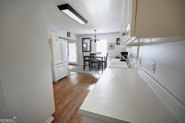 kitchen with a sink, freestanding refrigerator, white cabinetry, a textured ceiling, and dark wood-style floors