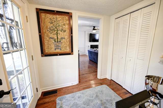 corridor with baseboards, a textured ceiling, visible vents, and wood finished floors