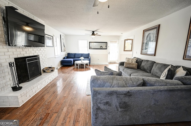 living area featuring wood finished floors, a textured ceiling, a brick fireplace, baseboards, and ceiling fan