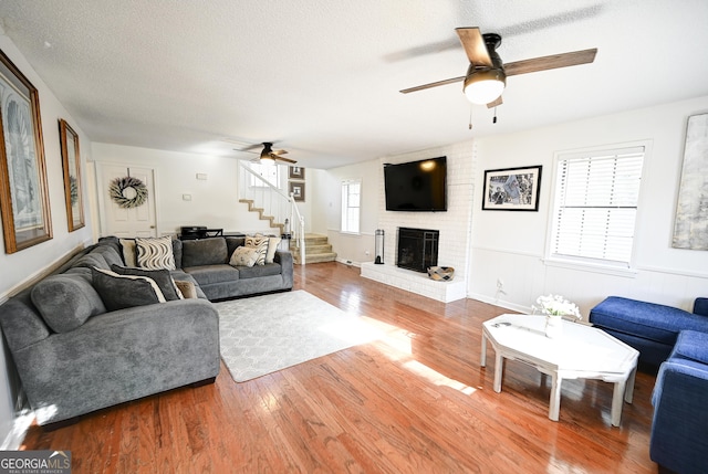 living room with a brick fireplace, stairway, a textured ceiling, a ceiling fan, and wood finished floors