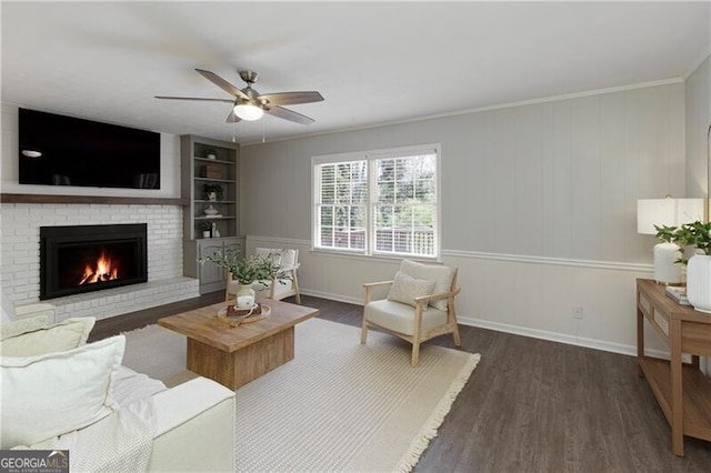 living room with wood finished floors, a brick fireplace, baseboards, ceiling fan, and ornamental molding