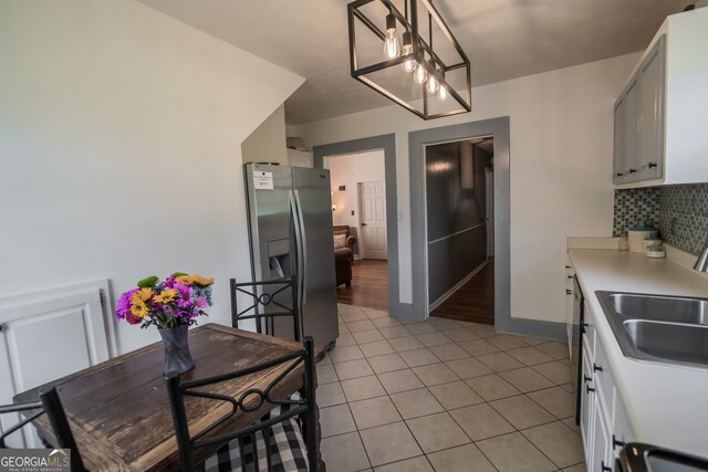 kitchen featuring light tile patterned flooring, decorative backsplash, stainless steel fridge, a sink, and an inviting chandelier