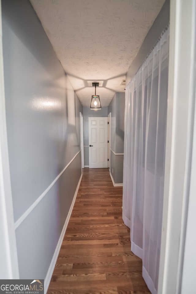 corridor with a textured ceiling, baseboards, and wood finished floors