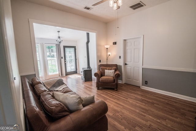 living room featuring ceiling fan with notable chandelier, visible vents, wood finished floors, and a wood stove