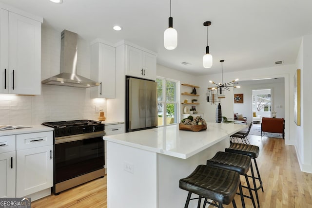 kitchen with light wood finished floors, wall chimney range hood, freestanding refrigerator, backsplash, and gas range oven