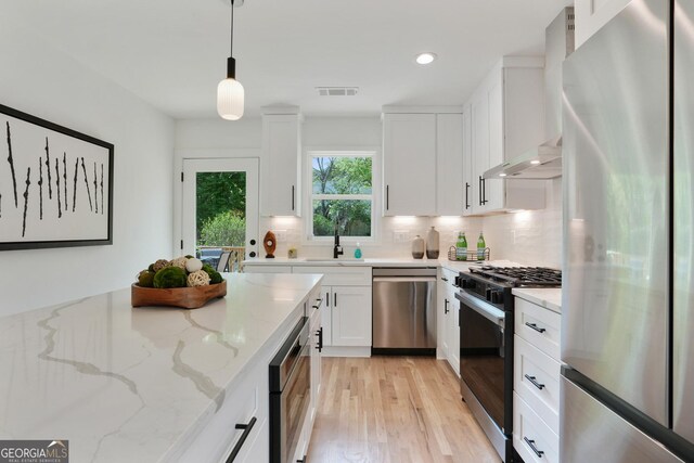 kitchen featuring wall chimney exhaust hood, tasteful backsplash, stainless steel appliances, visible vents, and white cabinets