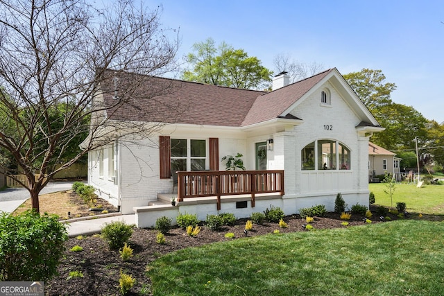 view of front of home featuring brick siding, a chimney, a front lawn, and roof with shingles