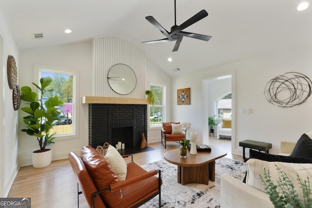living area with visible vents, light wood finished floors, a fireplace, a ceiling fan, and vaulted ceiling
