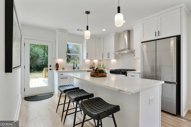 kitchen featuring tasteful backsplash, wall chimney exhaust hood, stove, and freestanding refrigerator