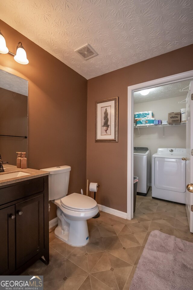 bathroom featuring washing machine and dryer, toilet, vanity, a textured ceiling, and visible vents