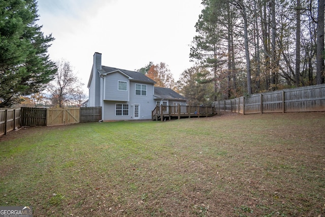 rear view of property featuring a gate, a chimney, a wooden deck, a fenced backyard, and a yard