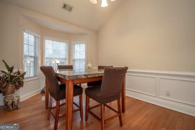 dining room with a wainscoted wall, a chandelier, lofted ceiling, light wood-style flooring, and visible vents