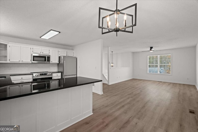 kitchen with open shelves, wood finished floors, stainless steel appliances, dark countertops, and white cabinets