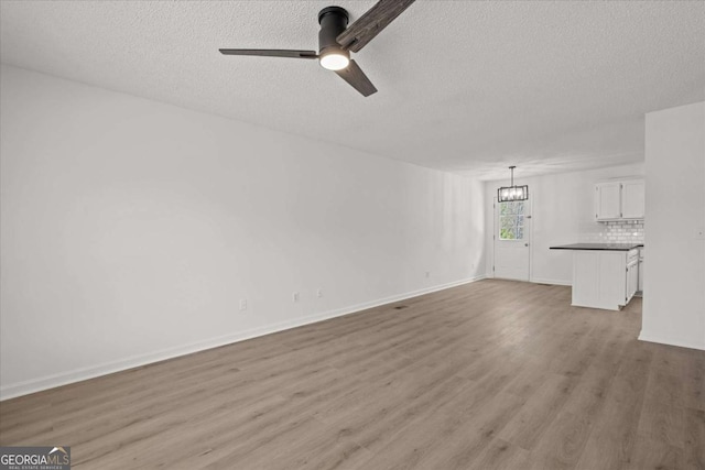 unfurnished living room with ceiling fan with notable chandelier, baseboards, a textured ceiling, and light wood-type flooring
