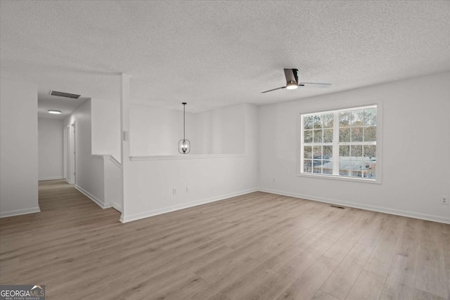 empty room with a ceiling fan, wood finished floors, a textured ceiling, baseboards, and visible vents