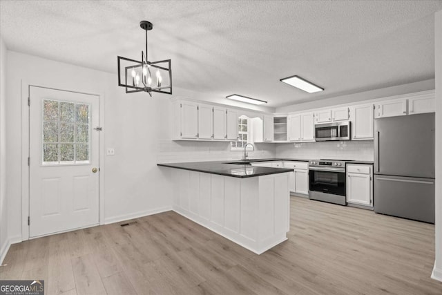 kitchen with a peninsula, light wood finished floors, stainless steel appliances, dark countertops, and a sink