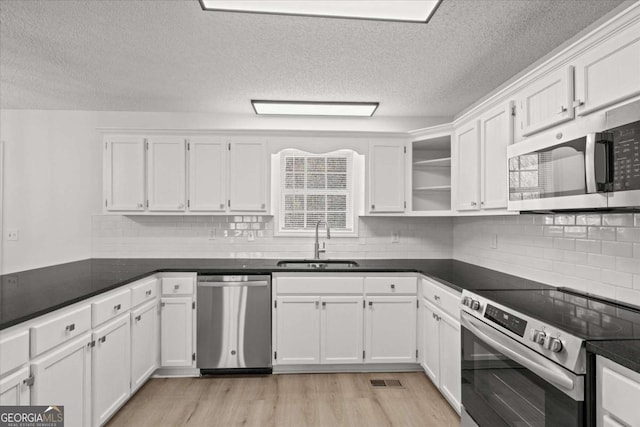 kitchen with a sink, open shelves, white cabinetry, stainless steel appliances, and dark countertops
