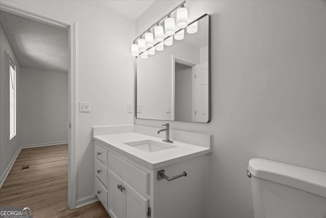bathroom with a textured ceiling, baseboards, toilet, wood finished floors, and vanity