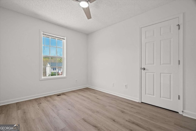 empty room featuring a ceiling fan, wood finished floors, a textured ceiling, baseboards, and visible vents