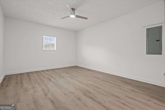 empty room with a textured ceiling, ceiling fan, wood finished floors, and electric panel