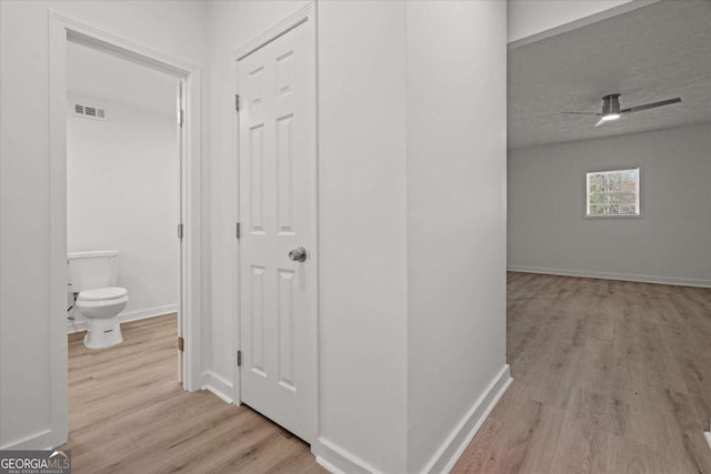 corridor featuring baseboards, a textured ceiling, visible vents, and wood finished floors