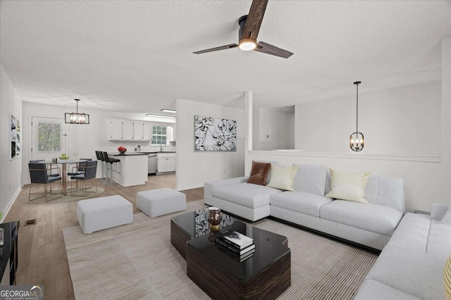 living room featuring ceiling fan with notable chandelier, light wood-style floors, baseboards, and a textured ceiling