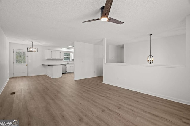 unfurnished living room with ceiling fan with notable chandelier, wood finished floors, baseboards, and a textured ceiling