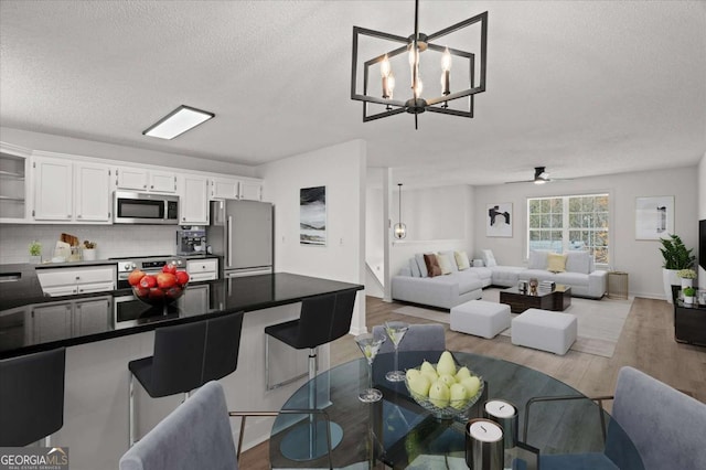dining area with a textured ceiling, light wood-style flooring, and ceiling fan with notable chandelier