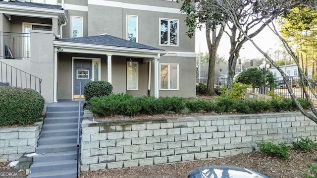 property entrance with a shingled roof, stucco siding, and fence