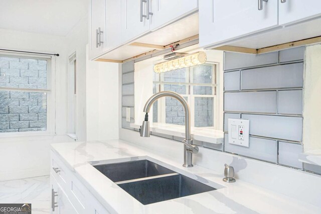 room details with white cabinetry, a sink, baseboards, and light stone counters