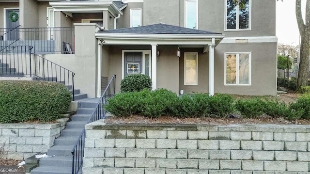 view of exterior entry featuring stucco siding and roof with shingles