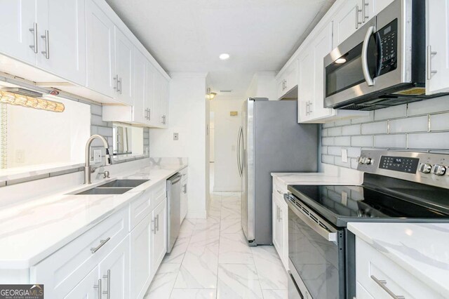 kitchen with a sink, white cabinetry, appliances with stainless steel finishes, marble finish floor, and decorative backsplash