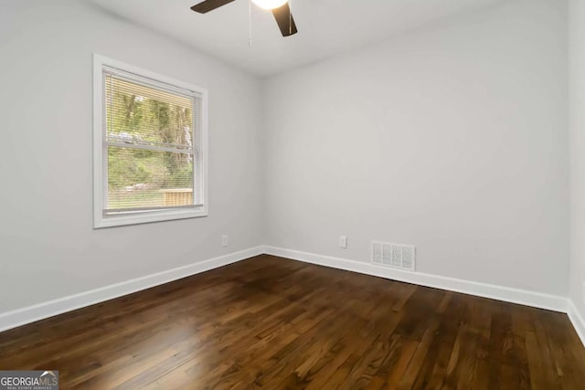 empty room with dark wood-style flooring, visible vents, baseboards, and a ceiling fan