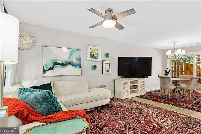 living area with ceiling fan with notable chandelier, baseboards, vaulted ceiling, and wood finished floors