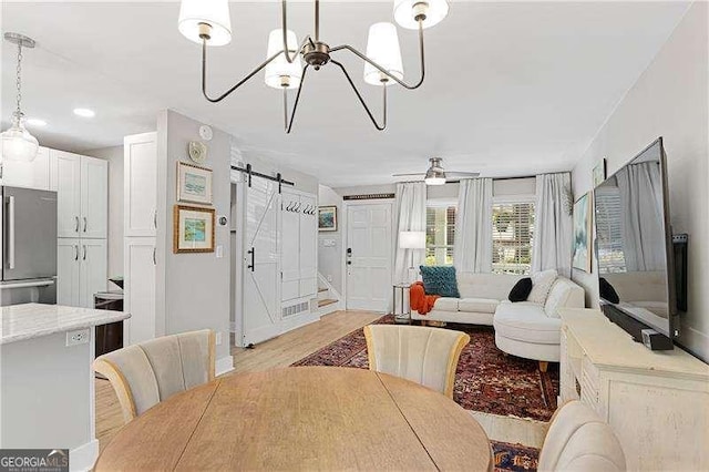 dining space with a barn door, ceiling fan with notable chandelier, and light wood finished floors