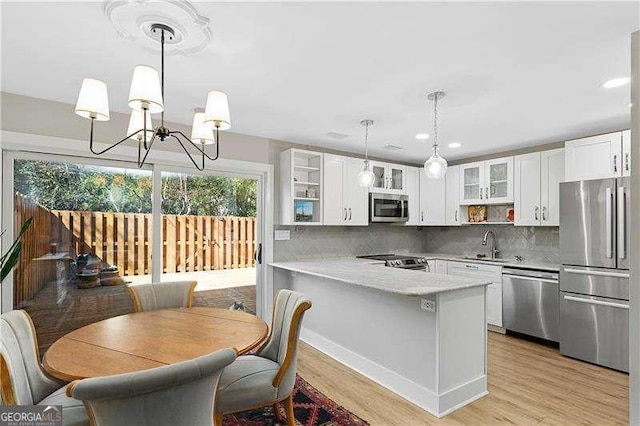 kitchen featuring a peninsula, stainless steel appliances, glass insert cabinets, light wood-style floors, and an inviting chandelier