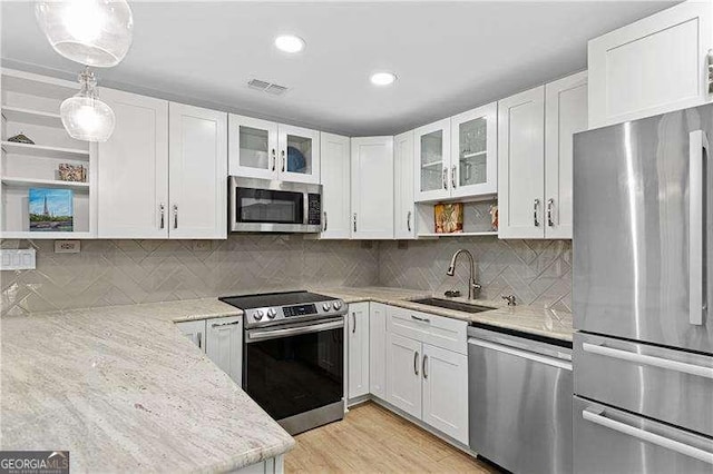 kitchen featuring a sink, open shelves, light stone countertops, stainless steel appliances, and white cabinets
