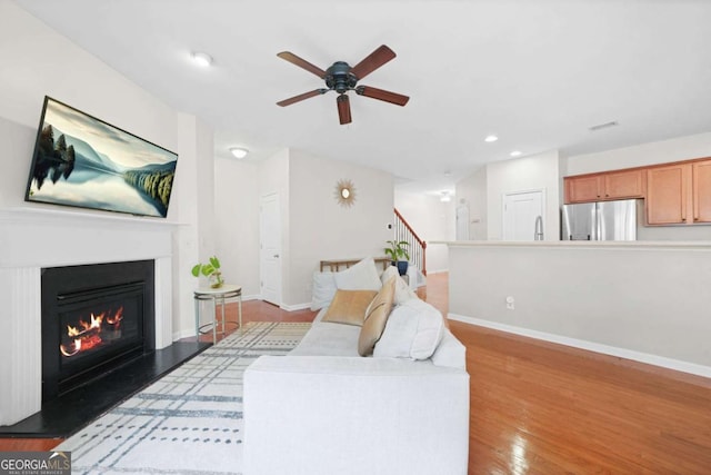 living area with light wood finished floors, baseboards, a glass covered fireplace, and a ceiling fan