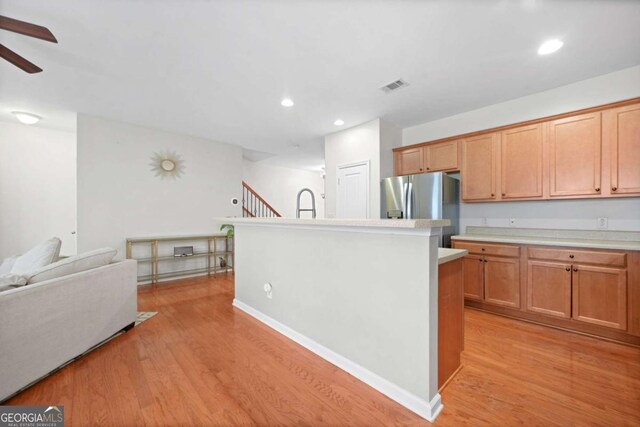 kitchen featuring light countertops, stainless steel fridge, a kitchen island with sink, visible vents, and light wood-style floors