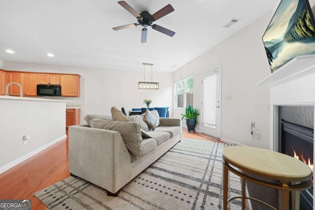 living room featuring recessed lighting, a lit fireplace, light wood-style floors, ceiling fan, and visible vents