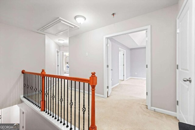 corridor with baseboards, an upstairs landing, attic access, and light carpet