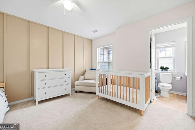 bedroom with visible vents, ceiling fan, a nursery area, light tile patterned floors, and light colored carpet