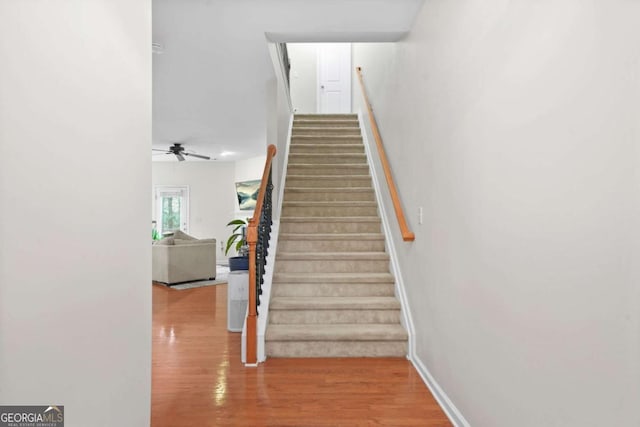 stairway featuring baseboards, wood finished floors, and ceiling fan