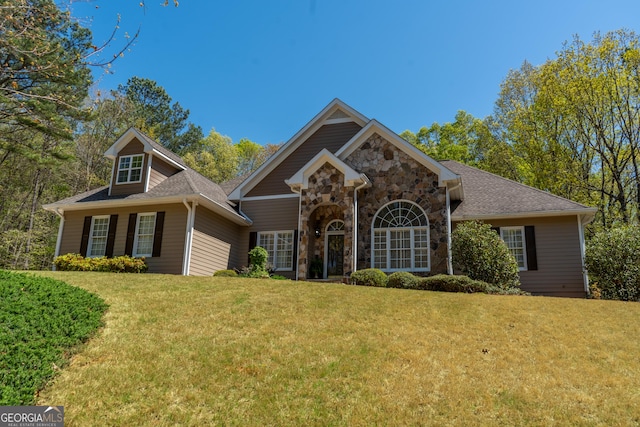 view of front facade with a shingled roof, stone siding, and a front lawn