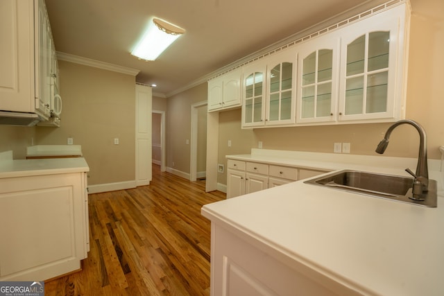 kitchen featuring wood finished floors, a sink, crown molding, baseboards, and glass insert cabinets