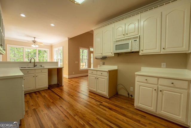 kitchen featuring wood finished floors, a sink, a wealth of natural light, crown molding, and white microwave