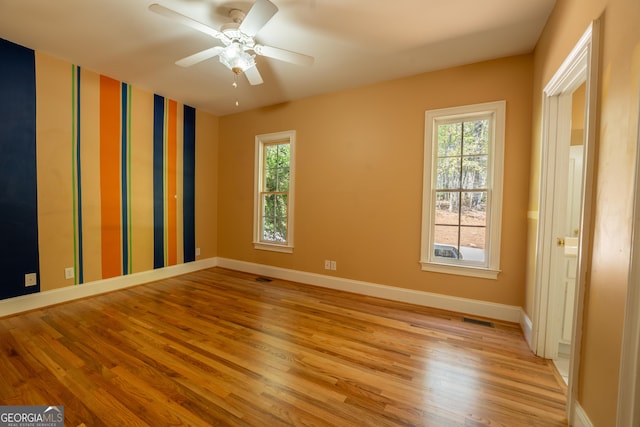 unfurnished room with a wealth of natural light, light wood finished floors, visible vents, and baseboards