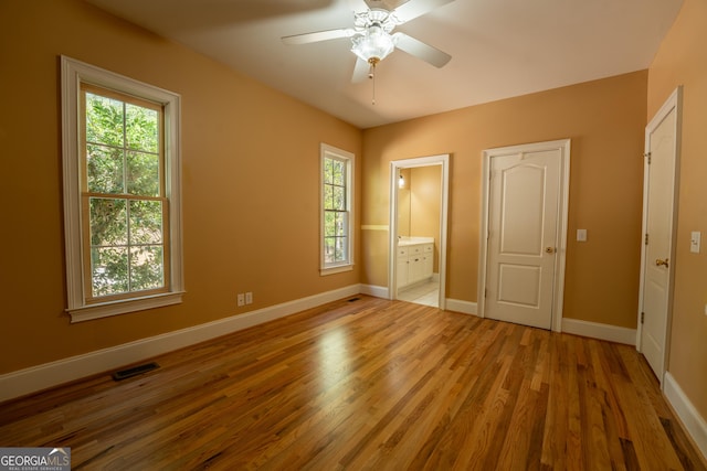unfurnished bedroom featuring baseboards, visible vents, a ceiling fan, wood finished floors, and connected bathroom