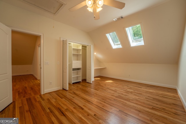 additional living space with visible vents, a ceiling fan, light wood-type flooring, attic access, and vaulted ceiling with skylight