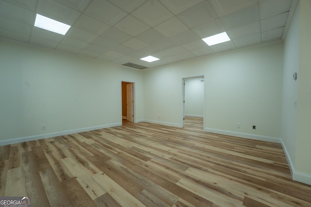 unfurnished room with light wood-type flooring, a drop ceiling, and baseboards